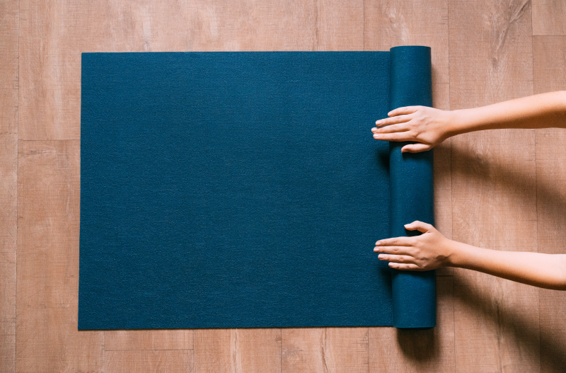 A person rolling up a dark blue yoga mat.