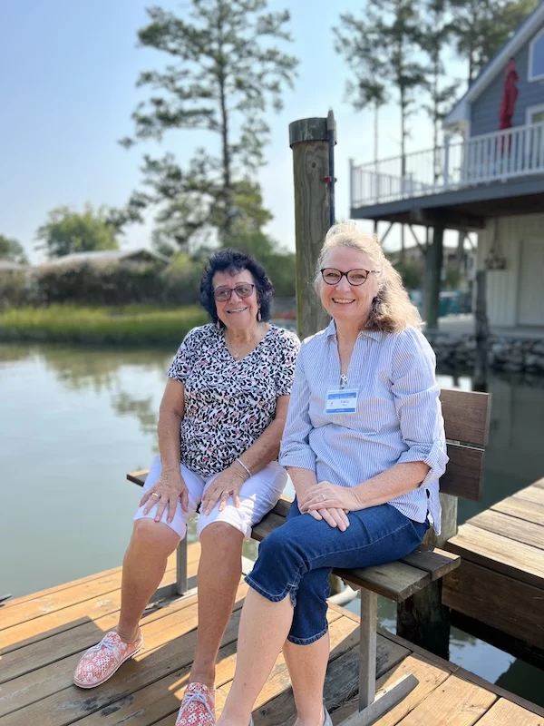 A Village Neighbors Volunteer sitting with a member on a dock over the water.