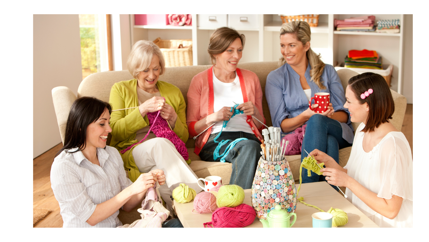 Five women sitting on a sofa, knitting.